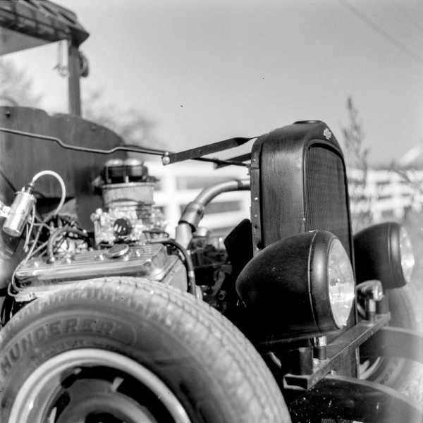Black and white photo of the side profile of an old hot rod Chevrolet with the engine hood removed and the engine gleaming in the sun, the bug eyed headlights protruding in the front and just the radiator standing proud held up with a couple extension arms. Looks to be a powerful beast. Shot with a Kiev 88 and ArsatC80f28 lens, on Kentmere100, and developed with FX-39II by Shom Bandopadhaya. Licensed under Creative Commons Attribution-NonCommercial-ShareAlike (CC BY-NC-SA).